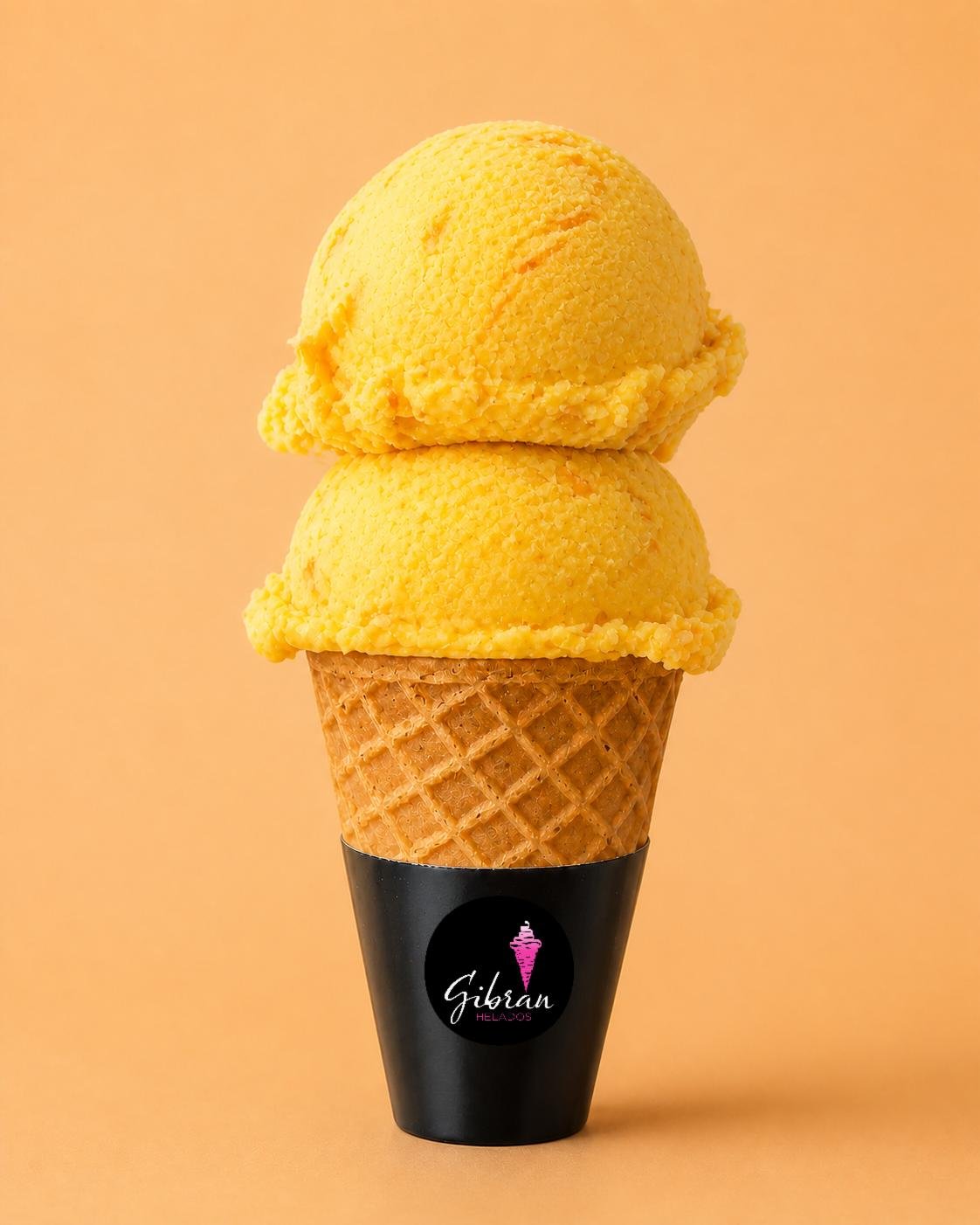 Cono de helado Mango Cempasúchil de Helados Gibran, CDMX. Sabor exclusivo de la membresía Helados Gibran. Desde $30 MXN la bola (2 bolas $50 MXN); litro $250 MXN (0.5 L $150, 4 L $950). Versión sin azúcar bajo pedido, endulzada con miel o fruta.